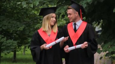 Kadın ve erkekte akademik elbiseler diploma tutarak, söz ve parkta yürüyüş