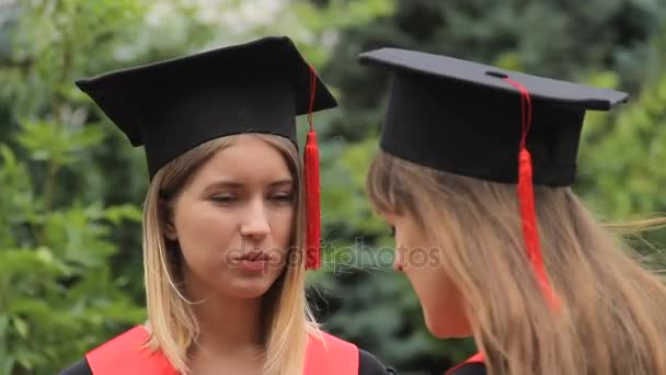 Duas mulheres graduadas em vestidos acadêmicos conversando após a cerimônia de formatura — Vídeo de Stock