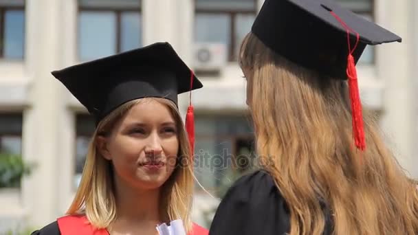 Blonde vrouw in academische GLB luisteren naar beste vriend bij graduatie ceremonie — Stockvideo