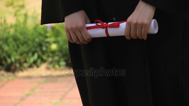 Handen van afgestudeerde holding diploma certificaat gebonden met rood lint, afstuderen — Stockvideo