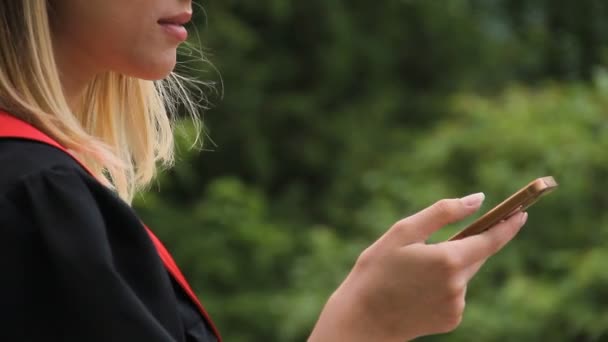 Счастливая выпускница читает сообщение по мобильному телефону, современные технологии — стоковое видео