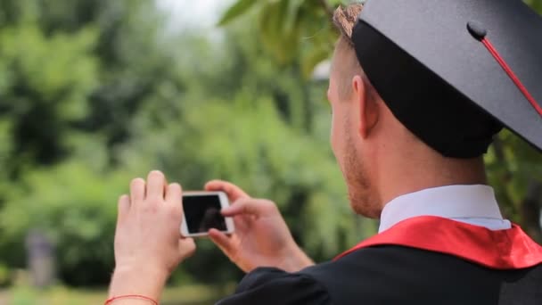 Man in academische jurk nemen van foto's van vrienden op de mobiele telefoon, graduatiedag — Stockvideo