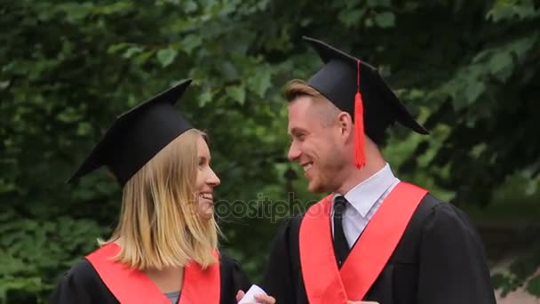 Preciosa pareja de estudiantes de pie en el parque y hablando, graduación, futuro feliz — Vídeos de Stock