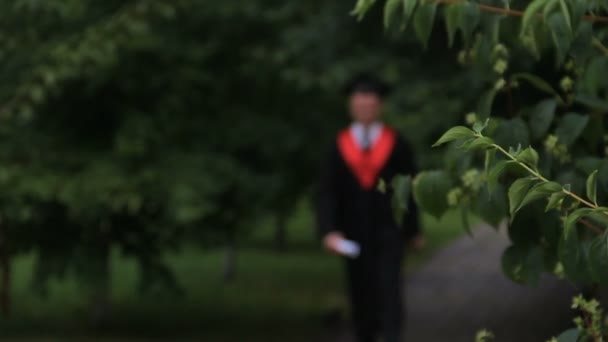 Studente di sesso maschile in abito accademico camminare e saltare con gioia nel parco, laurea — Video Stock