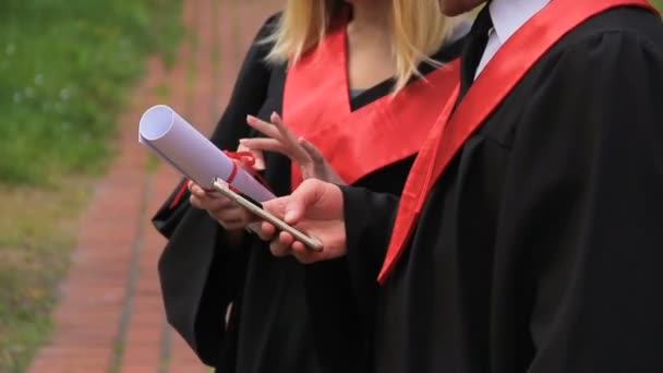 Amigos graduados navegando por las redes sociales en el teléfono inteligente, día de graduación — Vídeo de stock