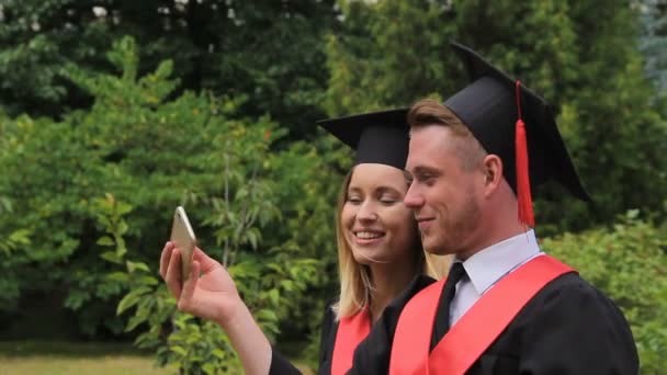 Usmíval se ženské a mužské absolventi drží diplomy a při selfie na telefonu — Stock video