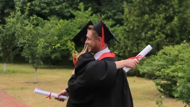 Blij vrouw en man in academische jurken omarmen na graduatie ceremonie — Stockvideo