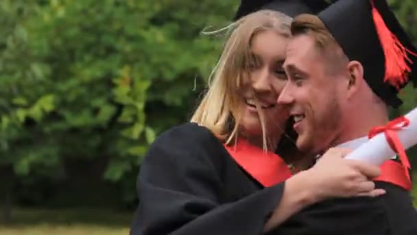 Sorrindo homem carregando amigo fêmea e dando a volta na cerimônia de formatura — Vídeo de Stock