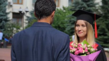Mezun kız arkadaşı tebrik ediyor ve çiçekler sunma takım elbiseli adam