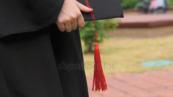 Giorno della laurea, studentessa in abito con cappuccio accademico e nappa in mano — Video Stock