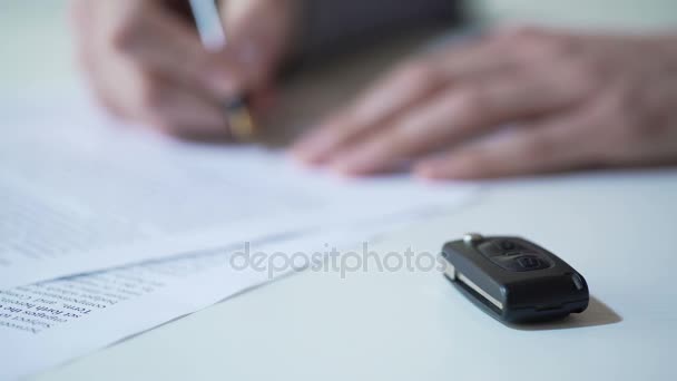 Man tekent papers over autoaankoop of huur, auto verzekeringen, sleutel op tafel — Stockvideo
