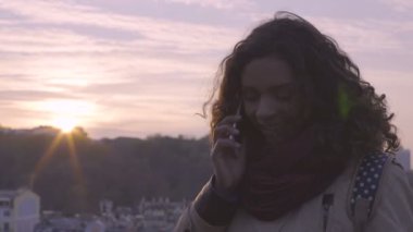 Gülümseyen ve telefon görüşmesinde gülüyor neşeli genç bayan şehir günbatımı