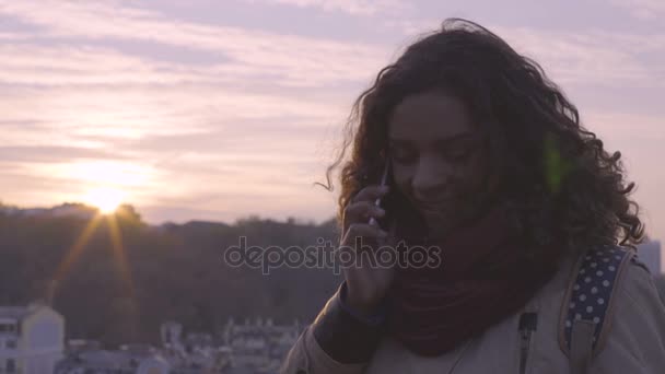 Vidám fiatal hölgy mosolyogva és nevetve a telefon beszélgetés közben város naplemente — Stock videók