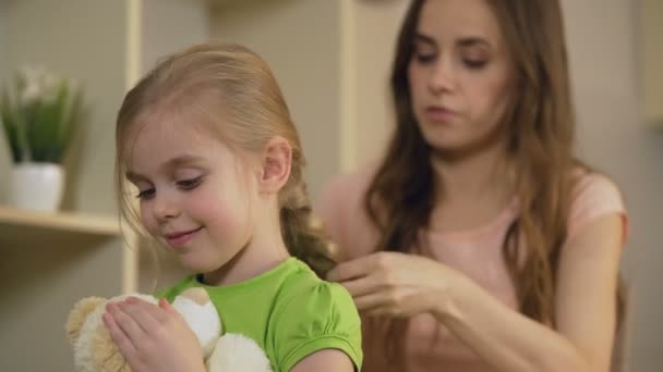 Mère souriante tressant joyeux cheveux petites filles, embrassant son enfant avec amour — Video