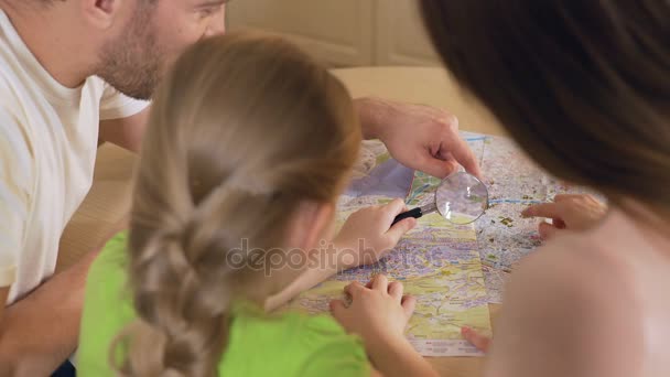 Glada far, mor och dotter tittar på karta genom förstoringsglas — Stockvideo