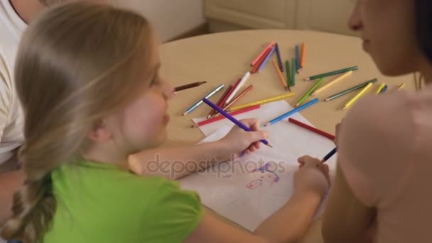 Little girl drawing family with colored pencils, mother and father helping her — Stock Video