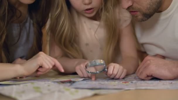 Родители учатся географии с дочерью, изучают карту через лупу — стоковое видео