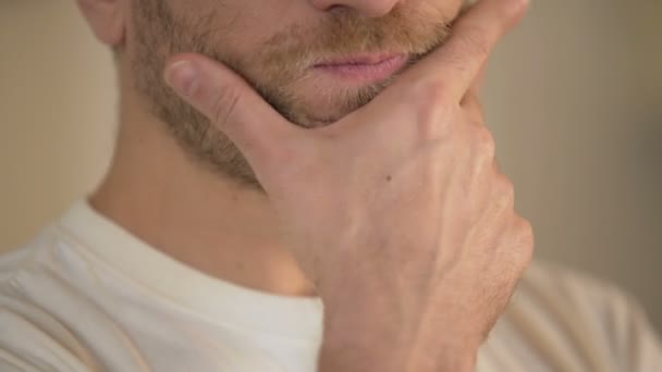 Крупним планом серйозний молодий чоловік з бородою натирає підборіддя, сумнівається, думає — стокове відео