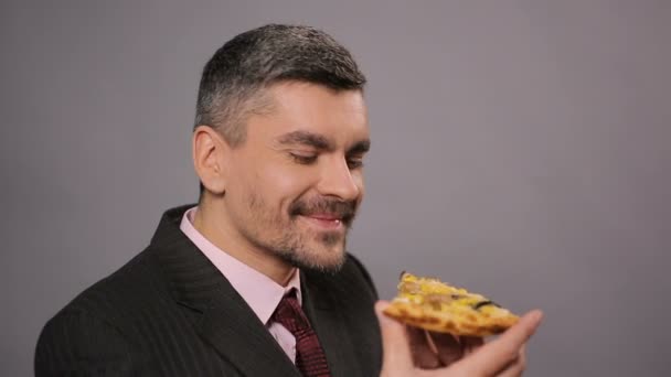 Hombre feliz en traje comiendo un pedazo de pizza sabrosa en el trabajo, comida grasa poco saludable — Vídeos de Stock
