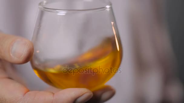 Main masculine secouant un verre avec du bourbon savoureux avant de l'essayer, super gros plan — Video