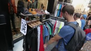 Genç adam malları satın almak seçme t-shirt ile sokak pazarında arıyorum