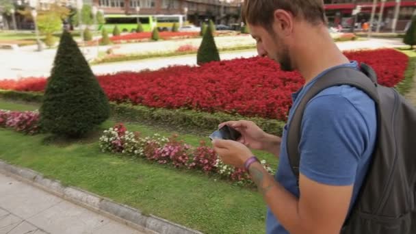 Человек стоит на городской площади и проверяет навигационное приложение, думая, куда пойти — стоковое видео