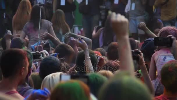 Grupo de personas felices lanzando pintura en polvo en el aire y filmando en el teléfono inteligente — Vídeos de Stock