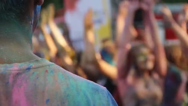 Hombre mirando el escenario y la gente bailando en el festival al aire libre Holi, relajación — Vídeo de stock