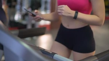 Koşu bandında egzersiz meşgul genç kadın spor, olarak çalışma sırasında Gadget'ı kullanma