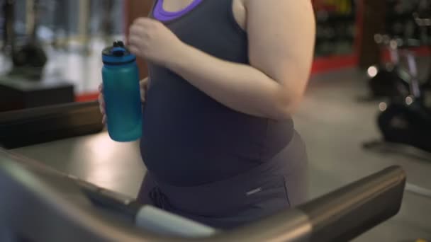 Femme en surpoids faisant de l'exercice sur tapis roulant, eau potable de bouteille, régime alimentaire — Video