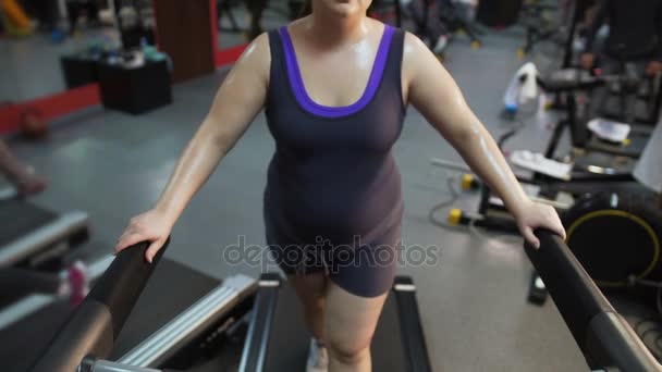 Молодая женщина с большим животом тренируется на беговой дорожке, упорно трудится, чтобы похудеть — стоковое видео