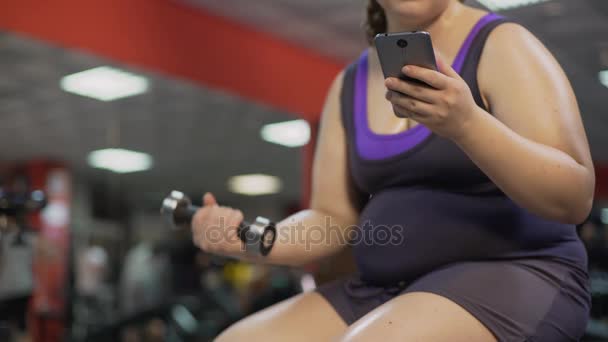 Mujer con sobrepeso usando la aplicación de fitness en gadget, haciendo ejercicio de mancuerna — Vídeo de stock