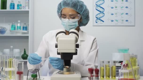 Лаборант смешанной расы проводит медицинские исследования, изучает микроскоп — стоковое видео