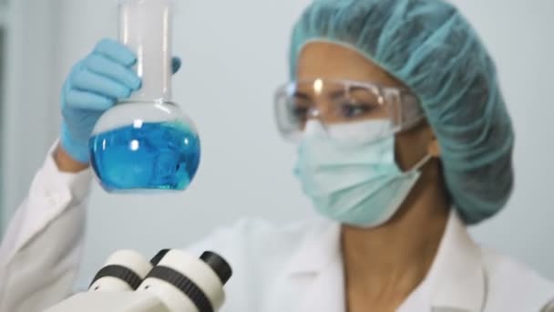 Интерн берет образец синей жидкости и проверяет его на микроскопе, в лаборатории — стоковое видео