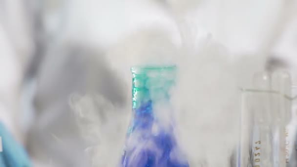 Синя рідина кип'ятіння і фумінг в колбі, студентка хімії проводять дослідження — стокове відео