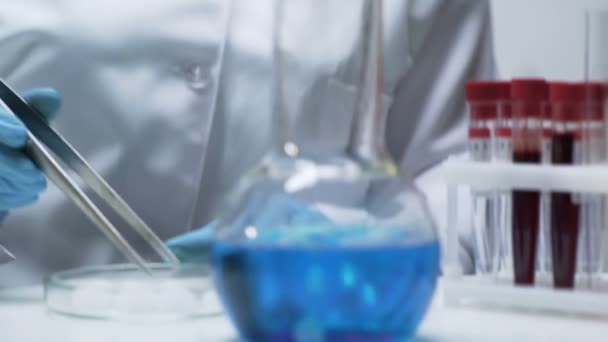 Assistente di laboratorio che aggiunge ghiaccio secco nel pallone con miscela blu brillante causando bolle — Video Stock