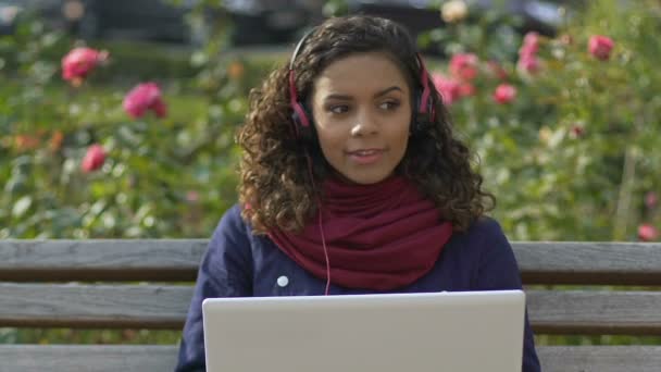 Hermosa chica multirracial en los auriculares escuchando música en el ordenador portátil, aplicación de audio — Vídeos de Stock