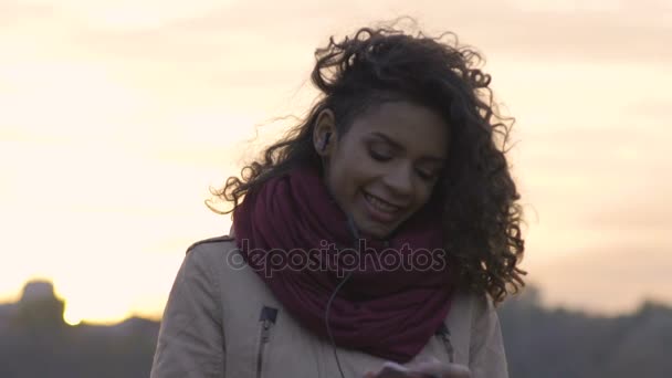 Νεαρό κορίτσι biracial χαμογελώντας, ακούγοντας την αγαπημένη μουσική σας σχετικά σύγχρονο gadget — Αρχείο Βίντεο