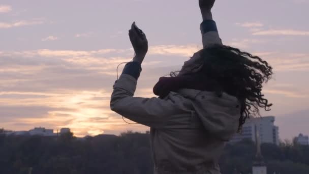 Молодая свободная счастливая женщина танцует на фоне городского пейзажа на закате — стоковое видео