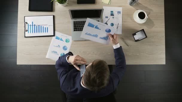 Persona d'affari guardando il grafico e parlando su smartphone, vista dall'alto sul posto di lavoro — Video Stock