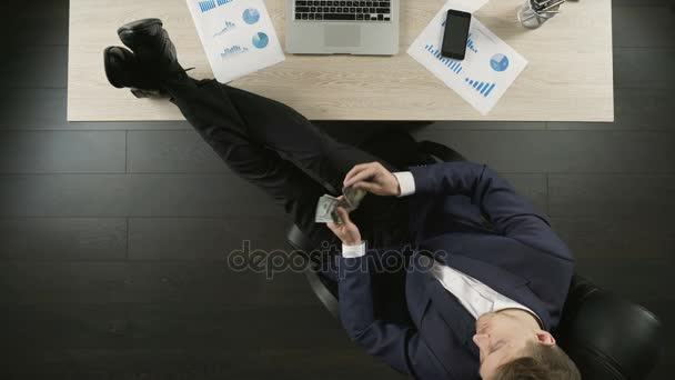 Χαλαρή πλούσιος επιχειρηματίας καταμέτρηση χρημάτων, κάθεται με τα πόδια στο τραπέζι, το top view — Αρχείο Βίντεο