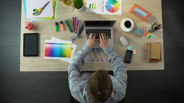 Diseñador creativo escribiendo en el ordenador portátil, enviando proyecto de arte al cliente, vista superior — Vídeo de stock