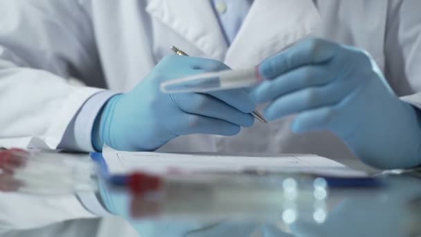 Trabajador de laboratorio rellenando formularios de resultados de pruebas, sosteniendo tubo de plástico con muestra de VIH — Vídeo de stock