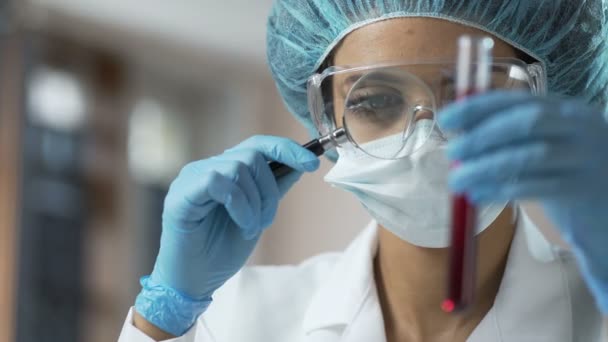 Женщина медицинский работник смотрит на анализ крови через увеличительное стекло, анализ — стоковое видео
