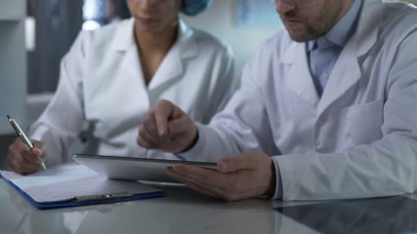 Männlicher Arzt hält Tablette in der Hand, gibt weiblichen Assistenten Anweisungen, sich Notizen zu machen — Stockvideo
