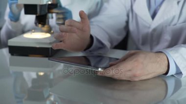Erkek bilim adamı tablet ekranı, mikroskop çalışma arkadaşı kaydırma