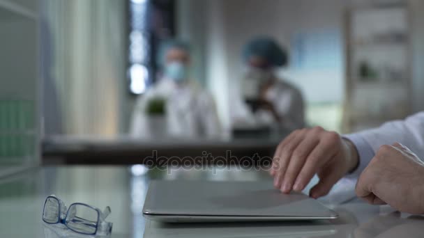 Un scientifique ouvre un ordinateur portable pour commencer à travailler sur un projet de recherche en laboratoire, médecine — Video