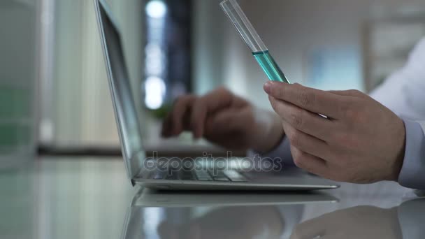 Tubo de retenção bioquímico com líquido turquesa, digitando resultados de teste no laptop — Vídeo de Stock