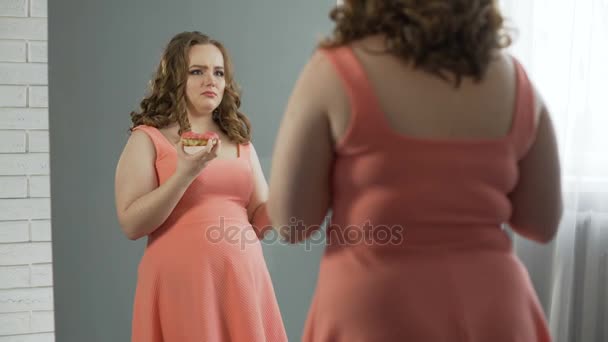 Депрессивная толстушка жует пончики перед зеркалом, у неё расстройство пищевого поведения — стоковое видео