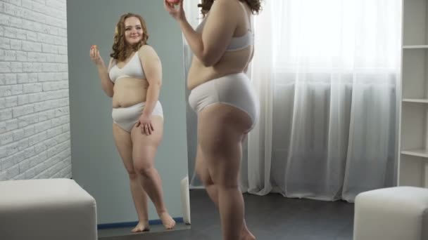 Тело позитивной девушки доволен своим весом, пожирает пончики перед зеркалом — стоковое видео